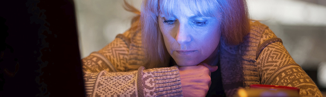 Middle-aged woman with Seasonal Affective Disorder (SAD) working at home on a laptop with an LED light shining on her, providing relief from seasonal depression.