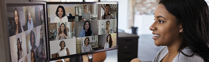 Woman attending virtual meeting and viewing other participants on two desktop monitors